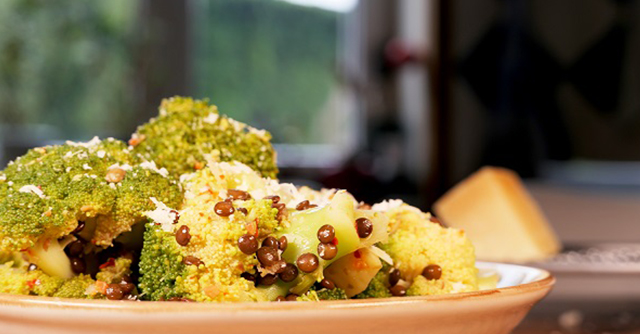 Brokkoli mit kleinen braunen Linsen vermischt auf einem hellen Teller.