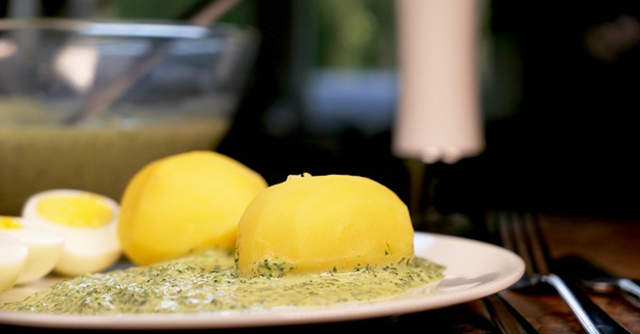 Zwei Kartoffel, zwei halbe gekochte Eier und grüne Soße auf einem weißen Teller.