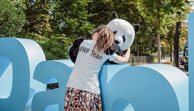 Ein Panda-Maskottchen und eine junge Frau in einem "WWF Team"-T-Shirt umarmen einander.