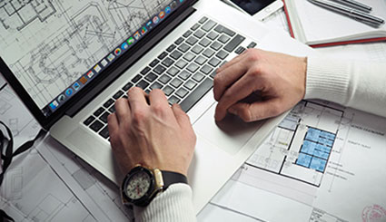 Männerhände ruhen auf der Tastatur eines Laptops, der Grundrisse zeigt.