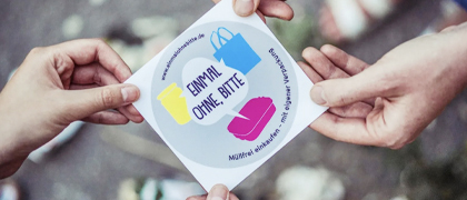 Zwei Paar Hände halten einen Sticker mit dem Logo des Projekts "Einmal ohne, bitte!
