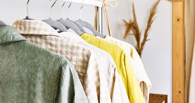 Eine Nahaufnahme einer Kleiderstange mit 5 Kleidungsstücken. Diese sind in gelb, hellbrauner und grüner Farbe.