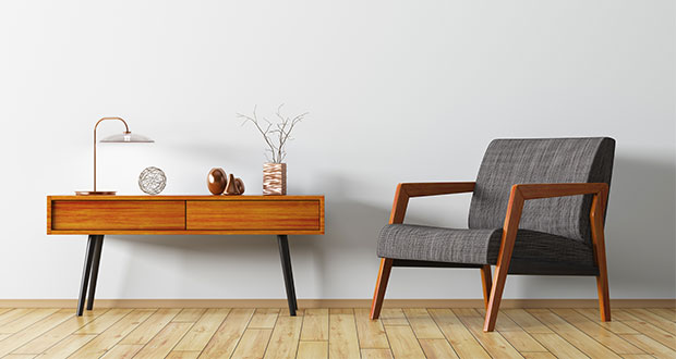 Ein Sessel aus braunem Holz mit einem dunkelgrauen Polster, daneben eine Kommode aus Holz mit einer Lampe und Dekoration.