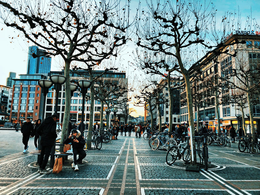 Ein Ausschnitt der Frankfurter Einkaufsstraße Zeil. Man sieht Fußgänger, Bäume und ein paar Gebäude