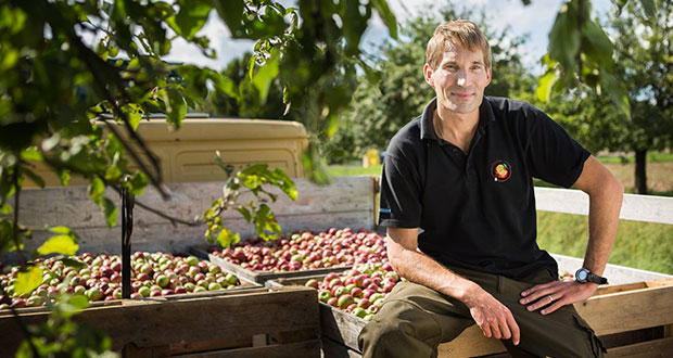 Peter Possmann sitzt auf einer Ladefläche eines LKWs, auf welcher sehr viele Äpfel geladen sind.