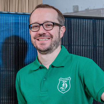 Portrait von Markus Schmid. Ein Mann mit grünem T Shirt, Brille und braunem Haar und Bart. Er lächelt in die Kamera.