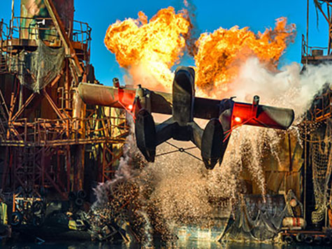 Eine Szene aus einem Action Film auf Netflix. Ein Flugzeug fliegt über Wasser, dahinter brennt etwas.