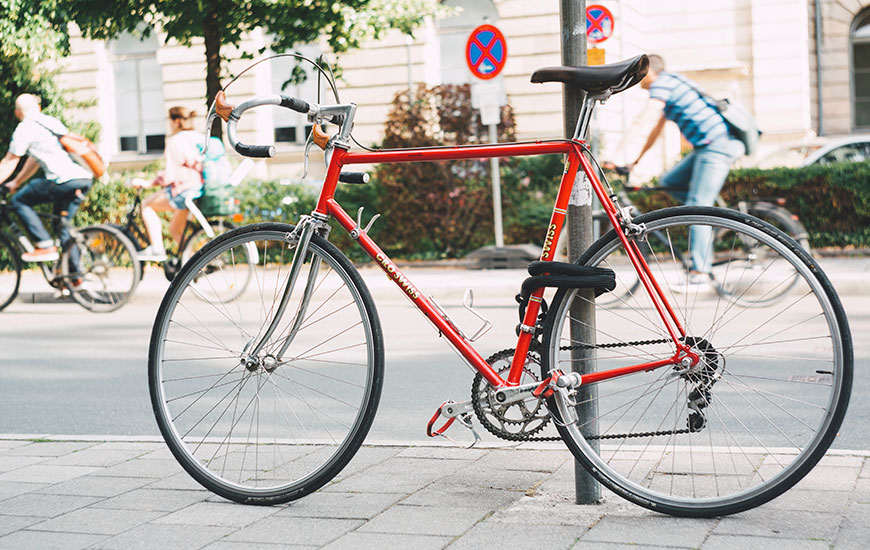 Ein rotes Rad lehnt an einem Pfosten. Dahinter sieht man Radfahrer über die Straße fahren