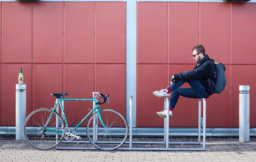 Ein Mann sitzt auf einem Fahrradständer, daneben steht sein Rad.